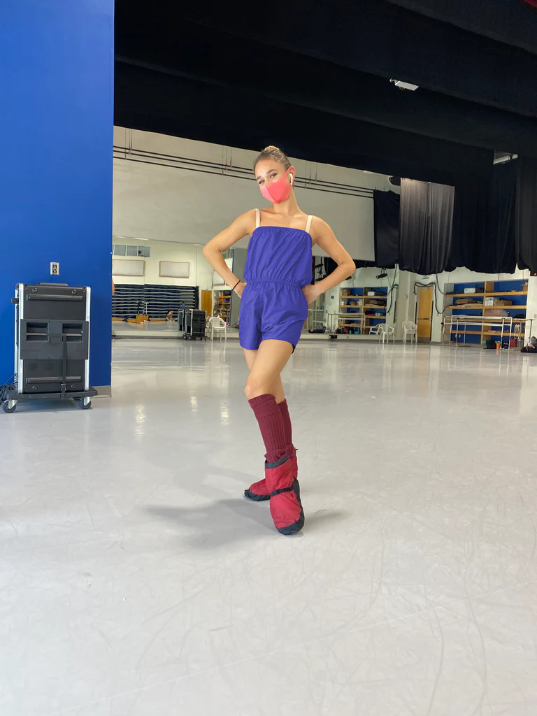 A dancer poses in a dance studio wearing a royal blue toned navy romper with a ruched waist.