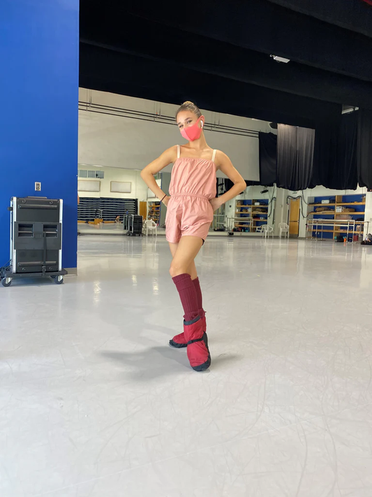A dancer poses in a dance studio wearing a peach romper with a ruched waist. 
