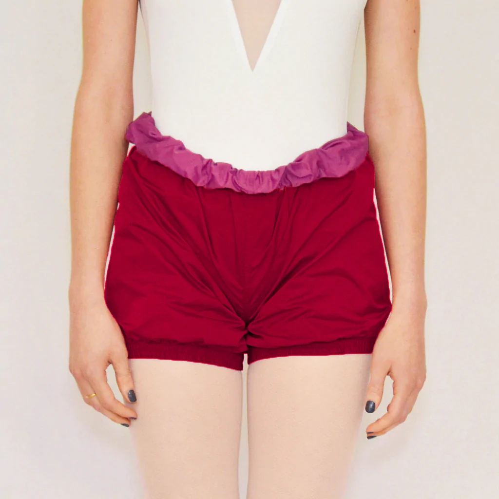 A dancer wears rose red trash-bag style shorts with a fuchsia waistband.